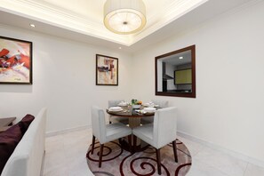 A dining area with a round table set for four, surrounded by chairs. There are two framed artworks on the walls, a ceiling light fixture, and a mirror on the wall.