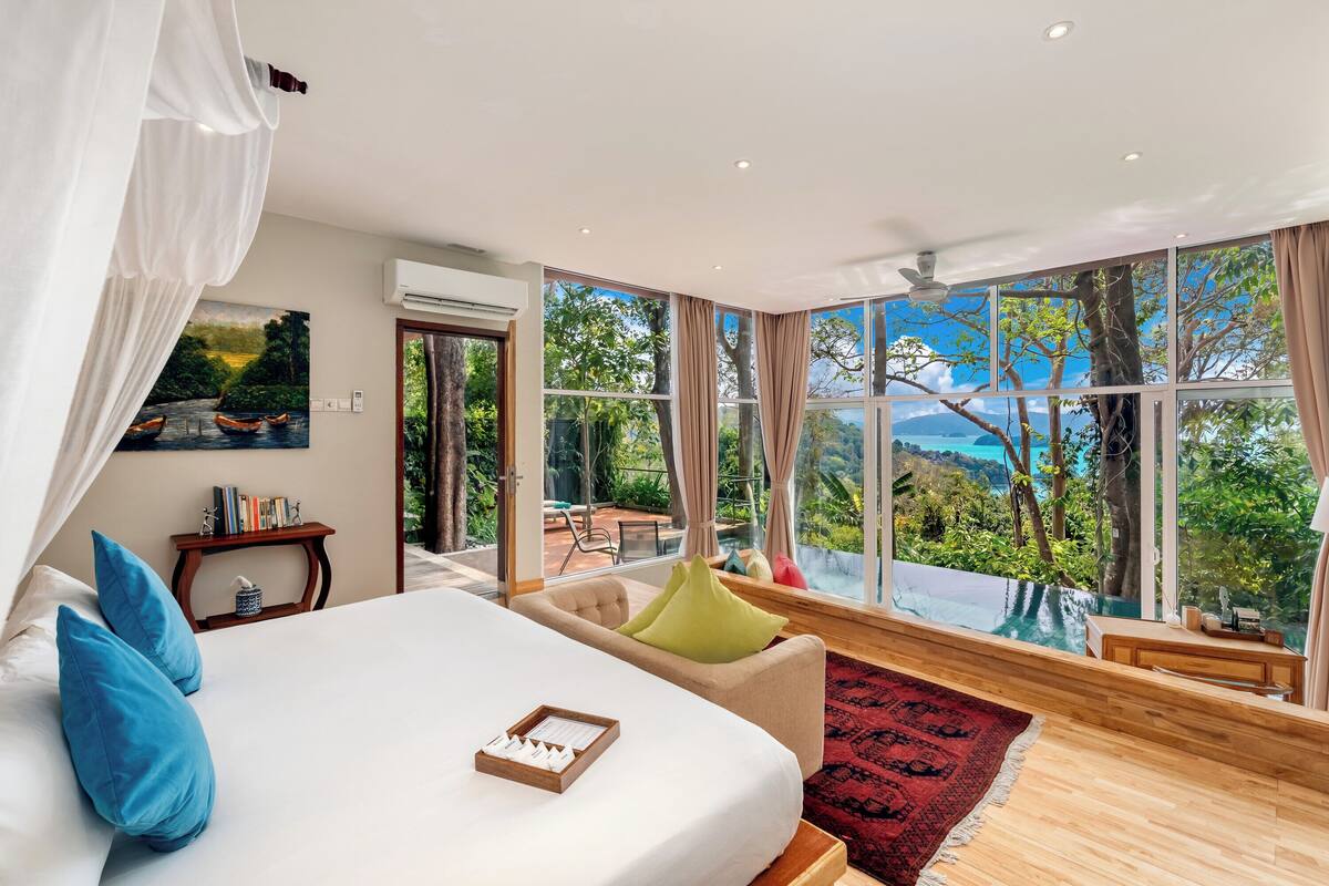 A bedroom with a large bed, a view of a pool, and a dining area.