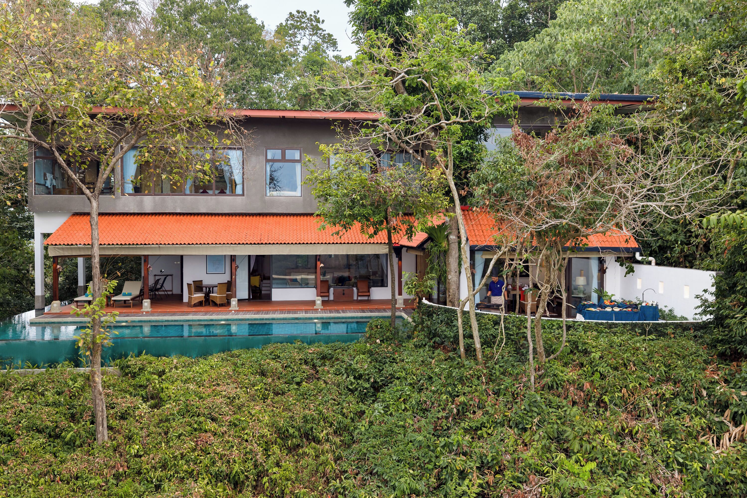 Uma casa de dois andares com piscina, cercada por vegetação densa.