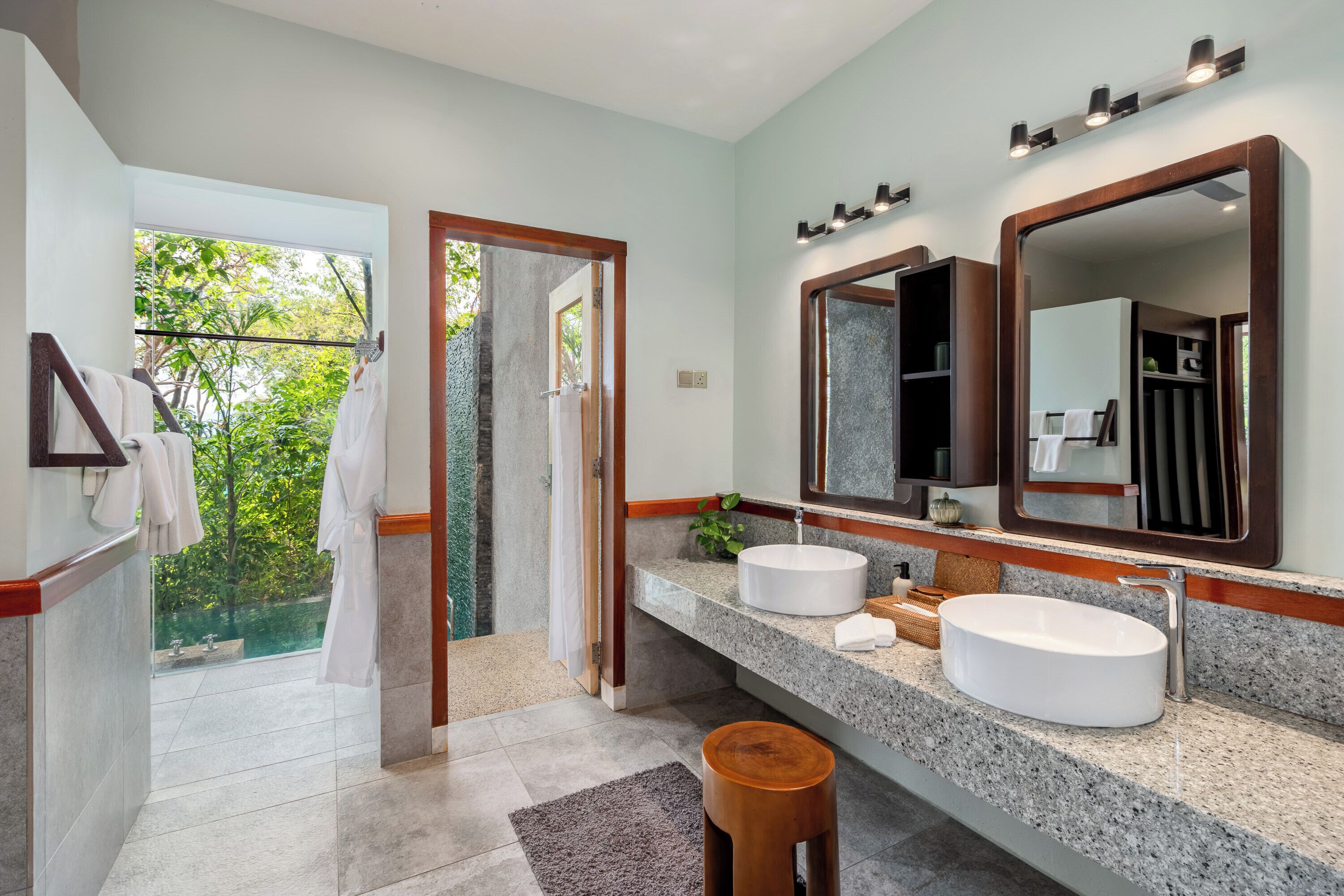 A bathroom with two sinks, a large mirror, and a view of greenery outside.