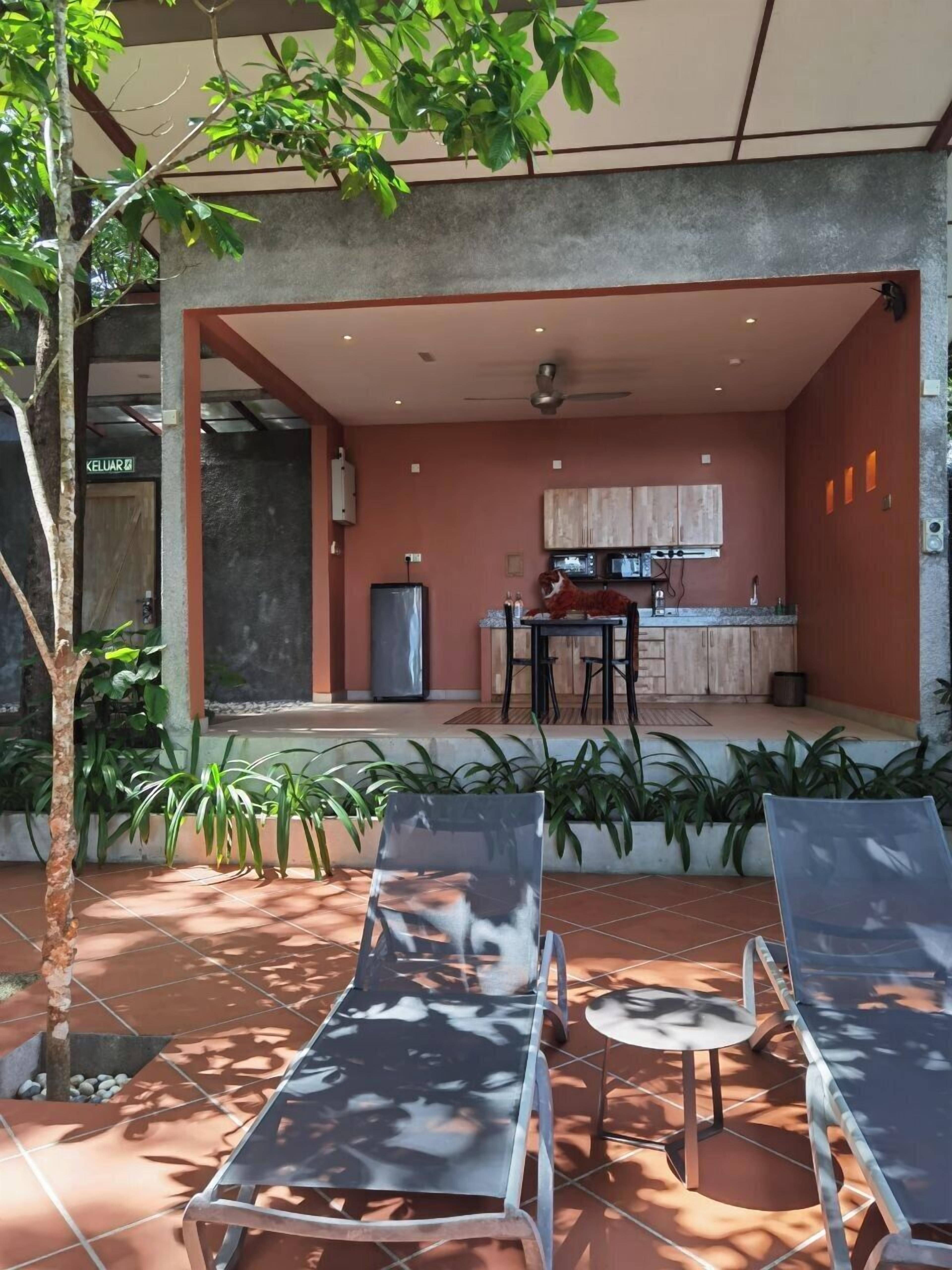 Un patio moderno al aire libre con dos sillones, una pequeña mesa redonda y una zona de cocina con armarios y un refrigerador.