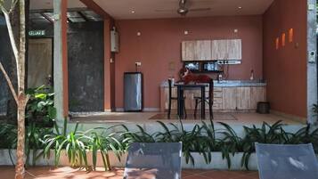Un patio moderno al aire libre con dos sillones, una pequeña mesa redonda y una zona de cocina con armarios y un refrigerador.