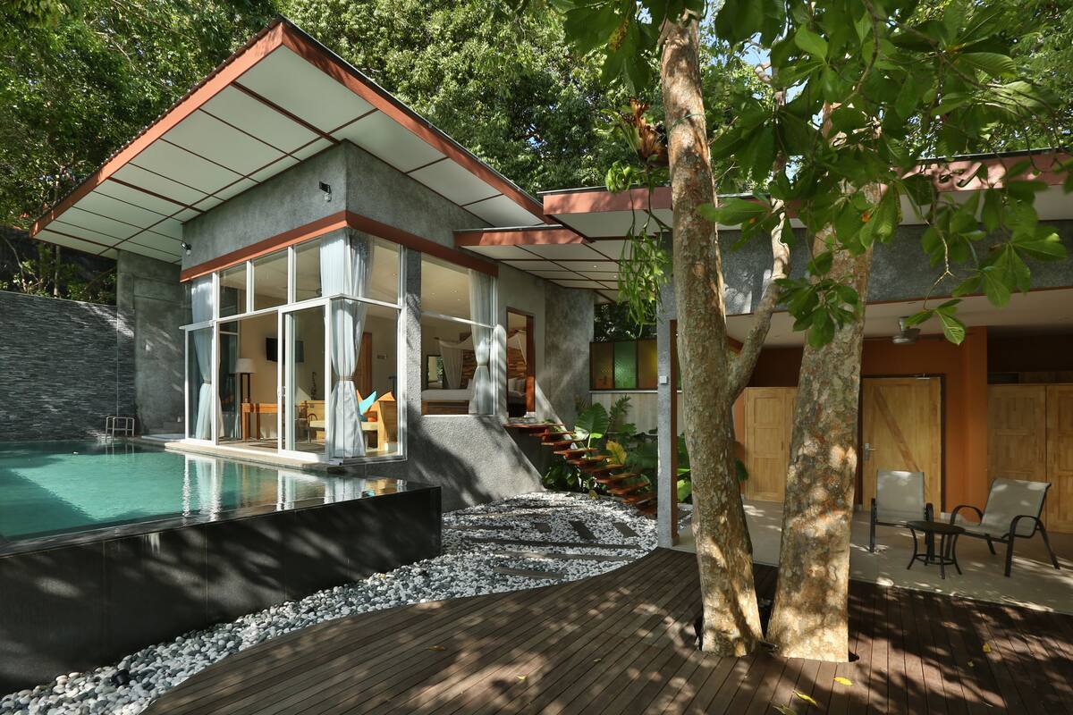 A modern house with a swimming pool, a wooden deck, and a staircase leading to a second level.