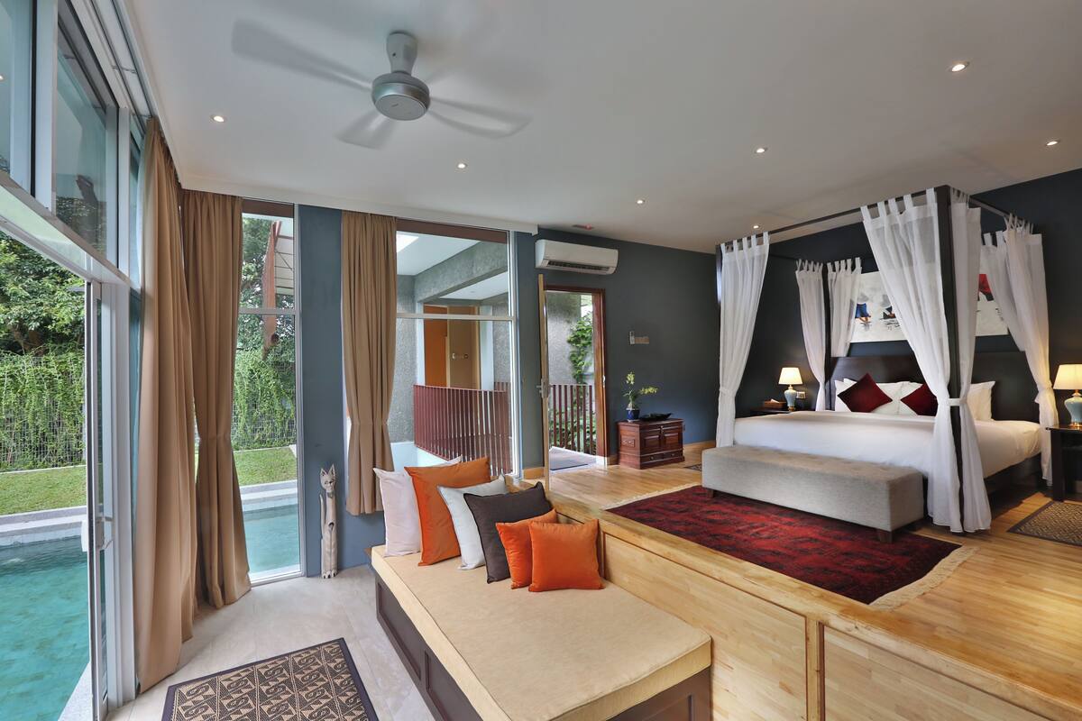 A bedroom with a large bed, a bench, and a view of a swimming pool.