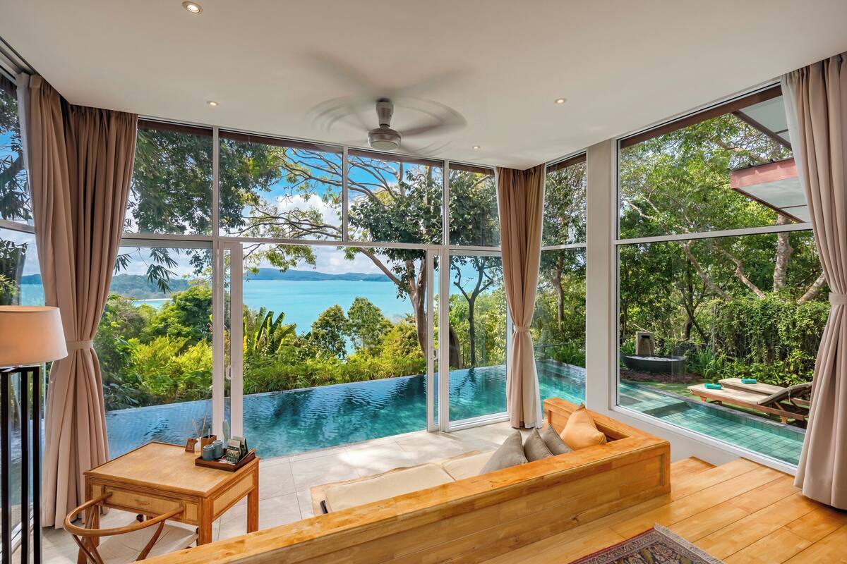 A room with a large window, a ceiling fan, a wooden bench, and a small table.