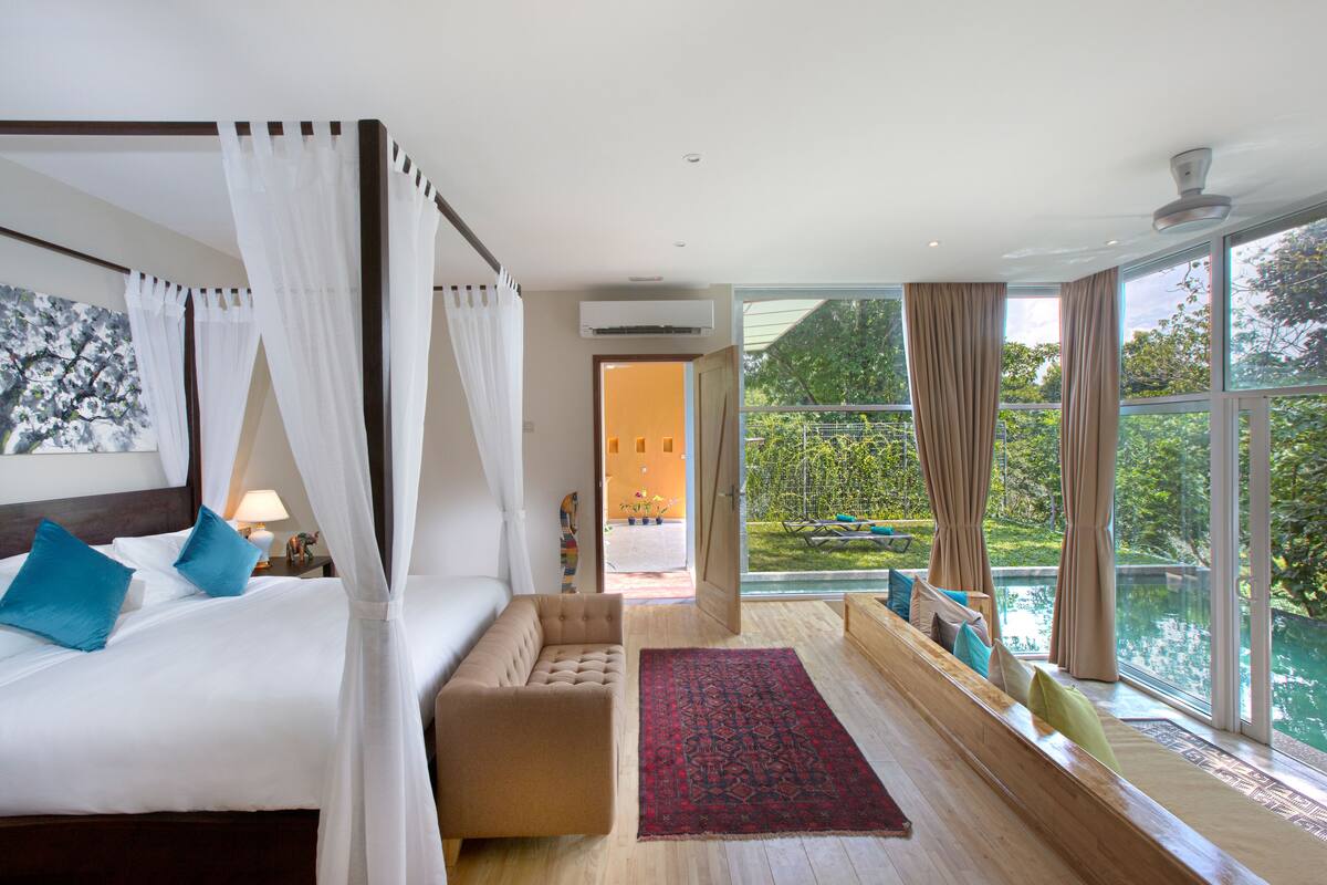 A bedroom with a large bed, a sitting area, and a view of a swimming pool.