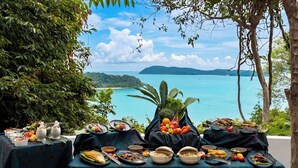 A table set with various dishes and a view of a coastal landscape. - Ambong Pool Villas (Langkawi)