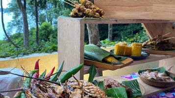 Diversas preparaciones a la parrilla de mariscos y verduras sobre una mesa de madera al aire libre, con un exuberante fondo verde.