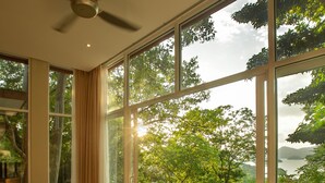 A bedroom with a bed, a desk, and a chair, large windows with a view of trees and water. - Ambong Pool Villas (Langkawi)