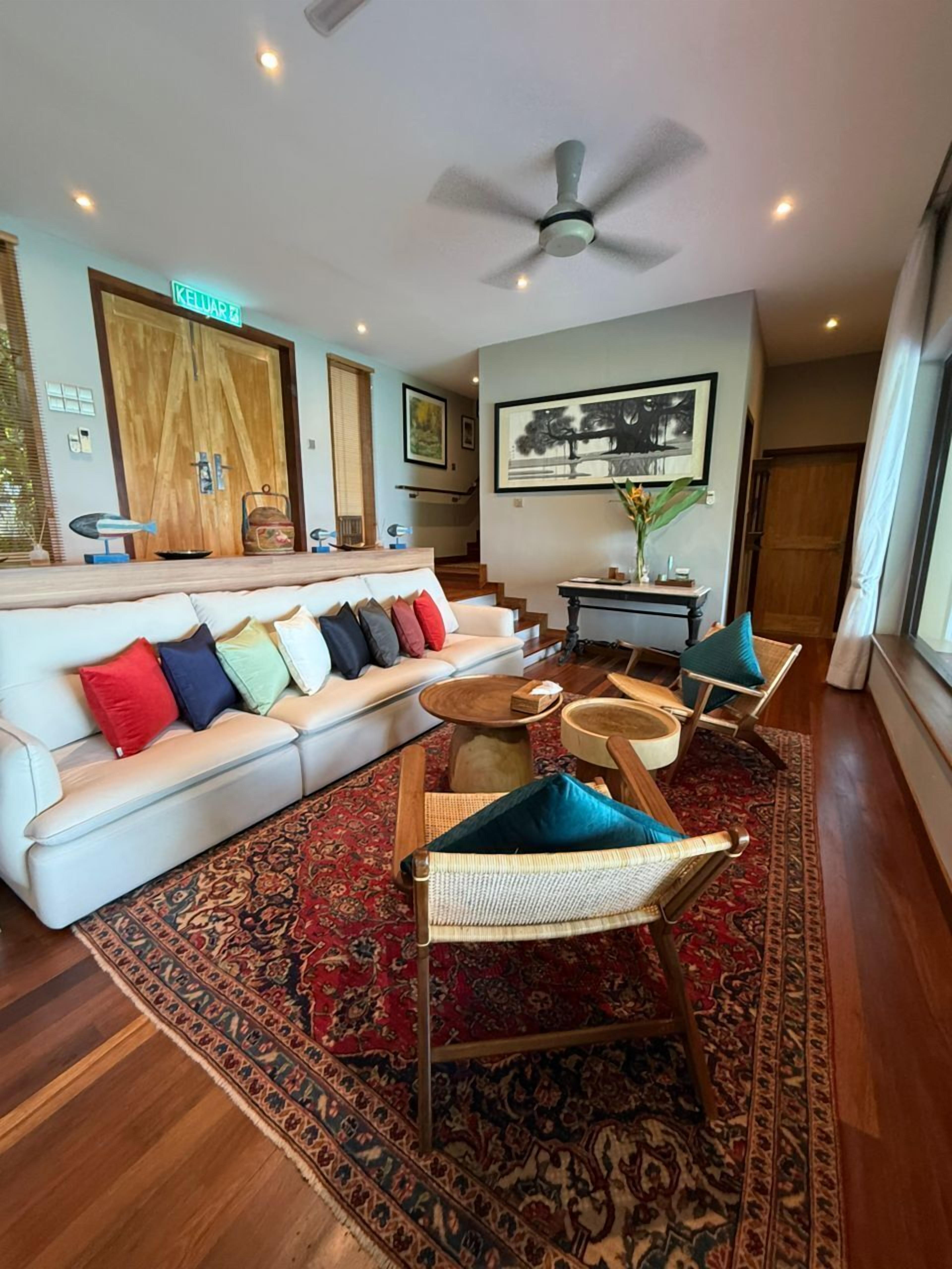 A spacious living room with a white sofa, colorful cushions, a wooden coffee table, and a large rug.