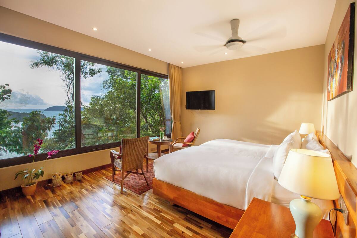 A hotel room with a large window, a bed, a desk, and a chair.