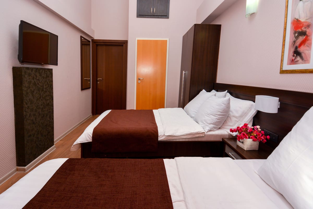 A hotel room with two beds, a TV, a wooden wardrobe, and a door.