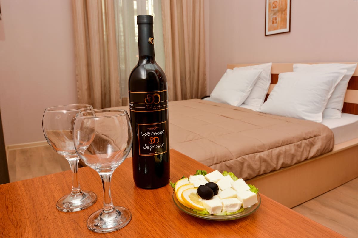 A hotel room with a bed, a table with a bottle of wine, two glasses, and a plate of cheese and olives.