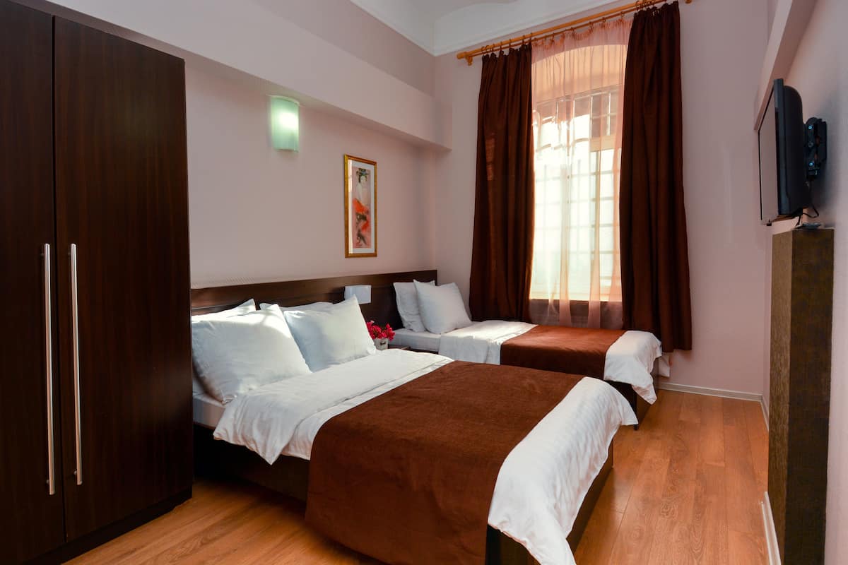 A hotel room with two beds, a wardrobe, a television, and a window with curtains.