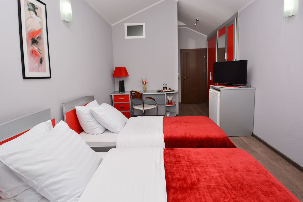 A hotel room with two beds, a desk with a chair, a TV on a cabinet, and a door leading to another room.