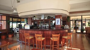 Zona de bar con un mostrador curvo, taburetes de madera y una variedad de botellas y vasos en estanterías.