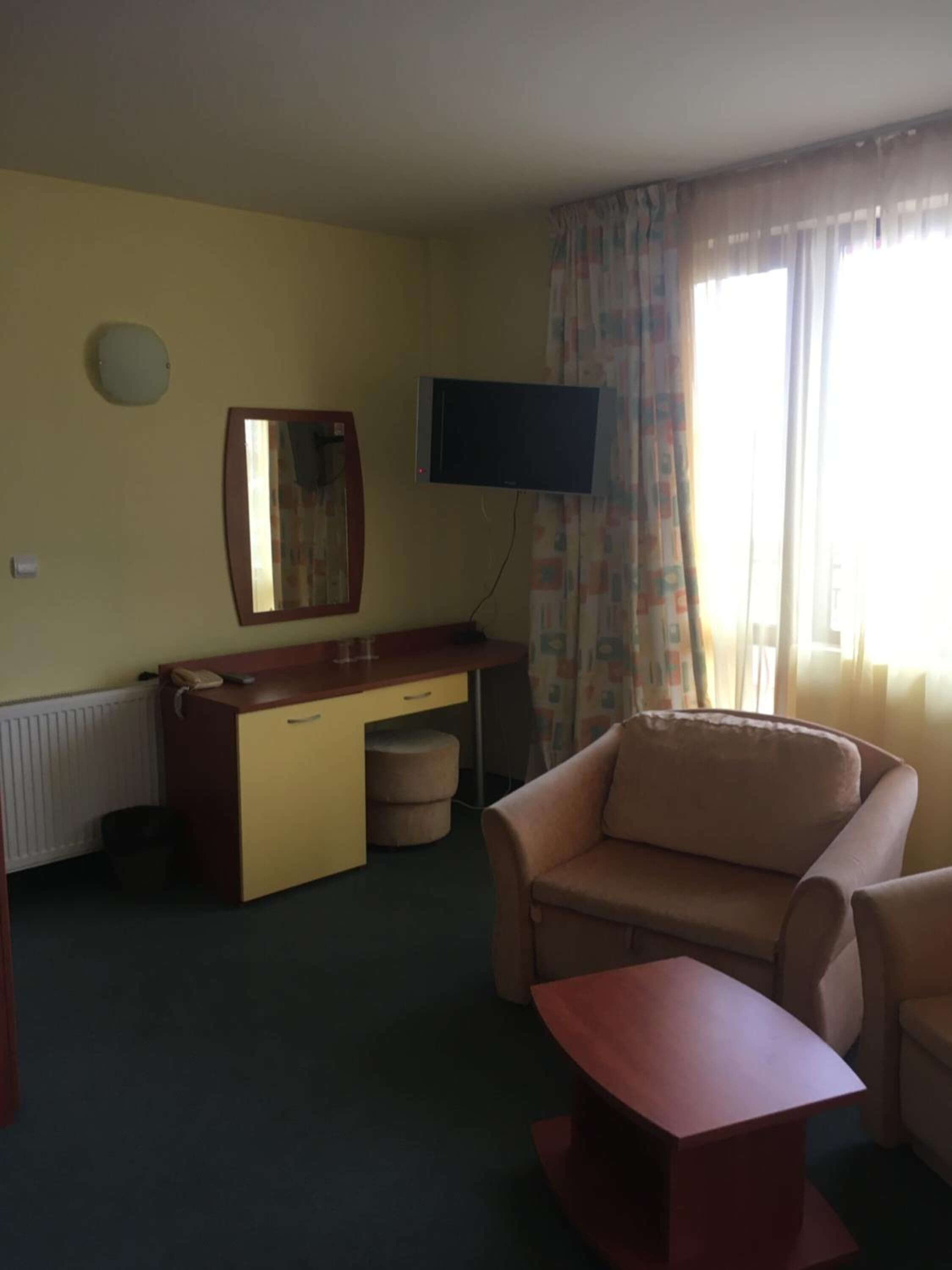 Una habitación con escritorio, sofá, televisión en la pared y ventana con cortinas.