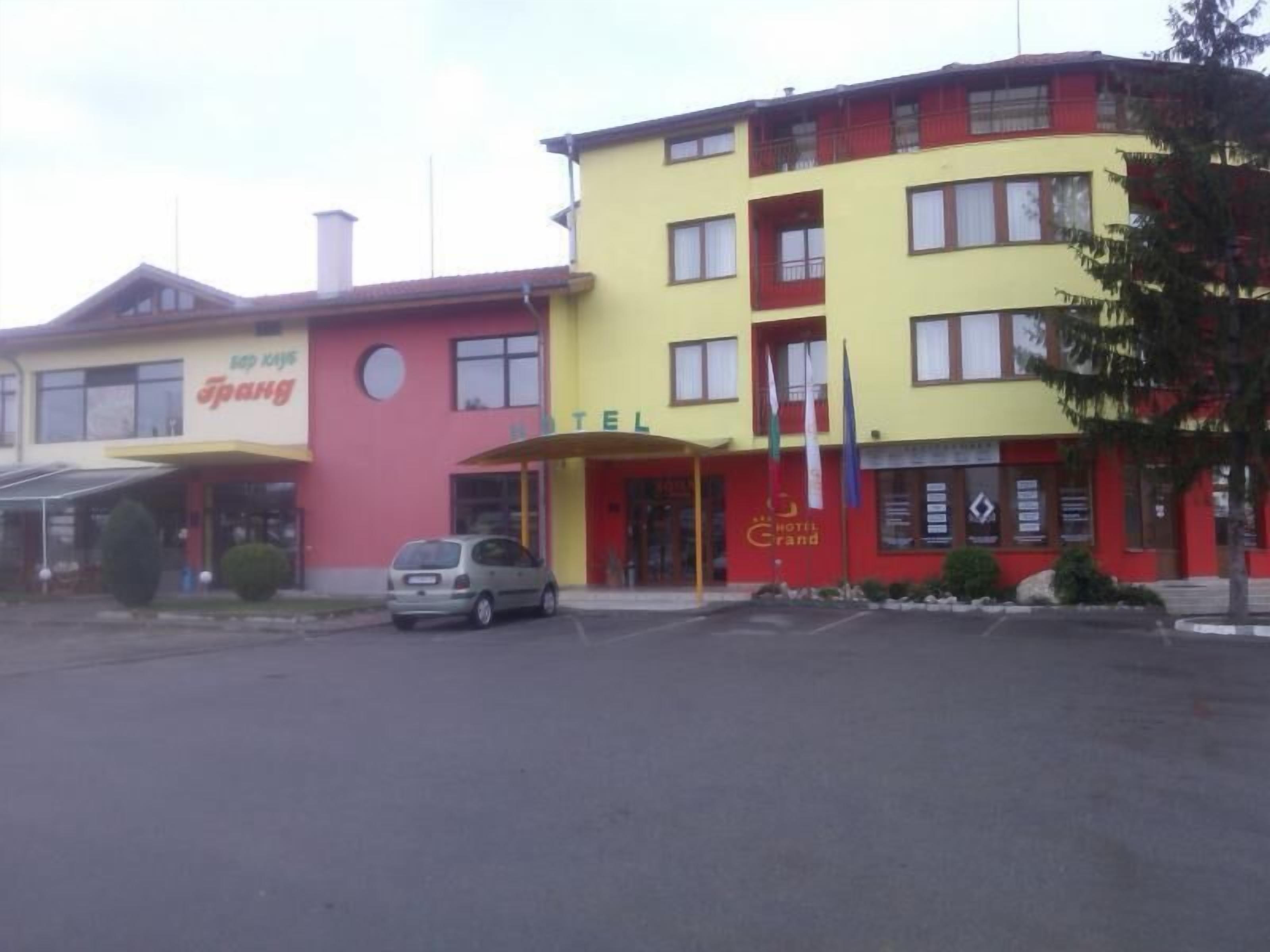 Un hotel amb façana vermella i groga, entrada ben visible i un cotxe aparcat al davant.