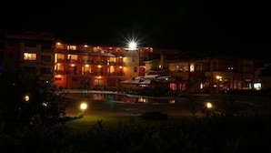 Un hotel de varios pisos con balcones iluminados y un área de piscina al frente.