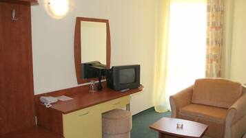 Une chambre d’hôtel de taille modeste, comprenant un bureau en bois, une télévision, une petite table, une chaise et une fenêtre avec des rideaux.