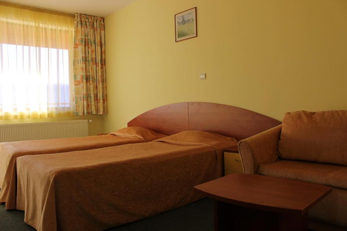Una habitación de hotel con dos camas individuales, un sofá, una mesita y una ventana con cortinas.