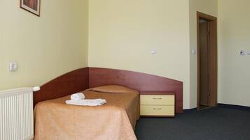 Un dormitorio pequeño y ordenado con una cama individual, una mesita de noche y una puerta.