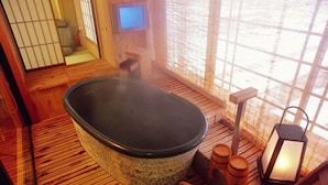 Een traditionele Japanse onsen met een stenen hottub, houten vloeren, een kleine televisie en een lantaarn.