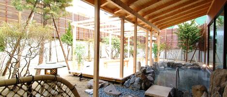A traditional Japanese garden with a wooden pergola, a hot spring, and a stone lantern.