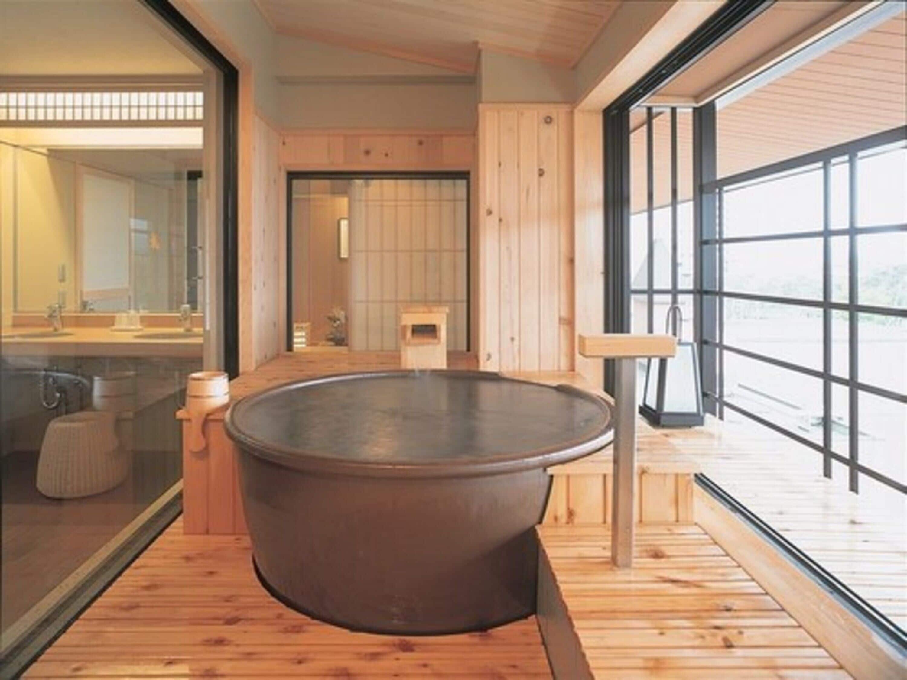 A modern bathroom with a large, round hot tub, wooden flooring, and large windows offering a view.