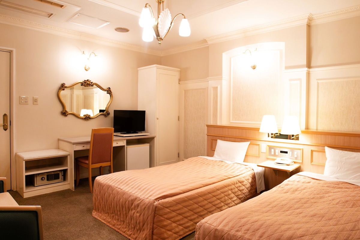 A hotel room with two beds, a desk, a television, and a mirror.
