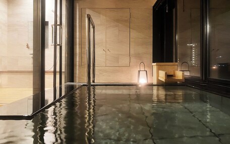 A modern indoor pool area with glass doors, a wooden bench, and a light fixture.