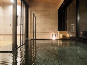 Un área interior de piscina moderna con puertas de cristal, un banco de madera y una lámpara.