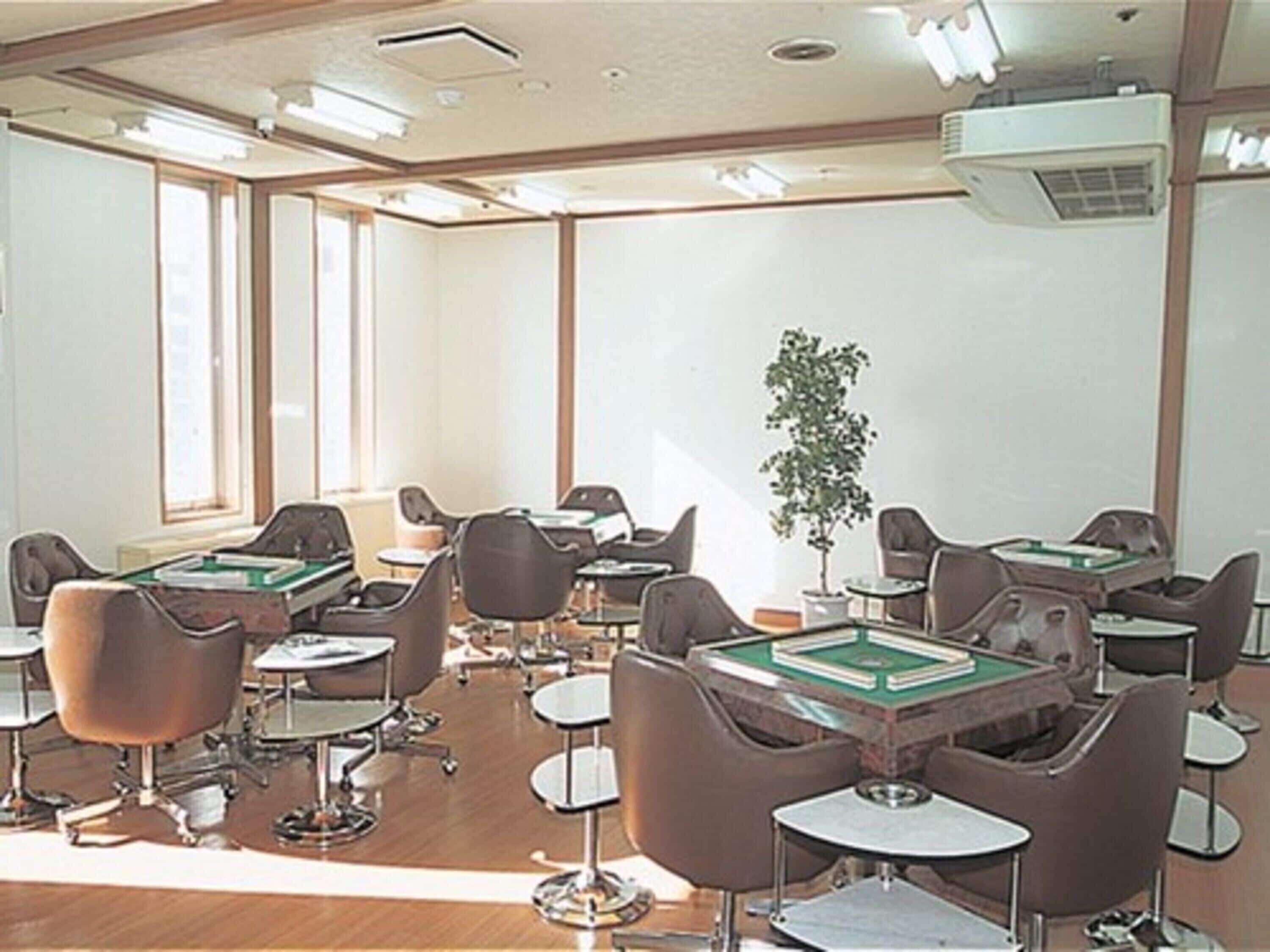 Un salón de conferencias con varias mesas y sillas, ventanas amplias y un equipo de aire acondicionado en el techo.