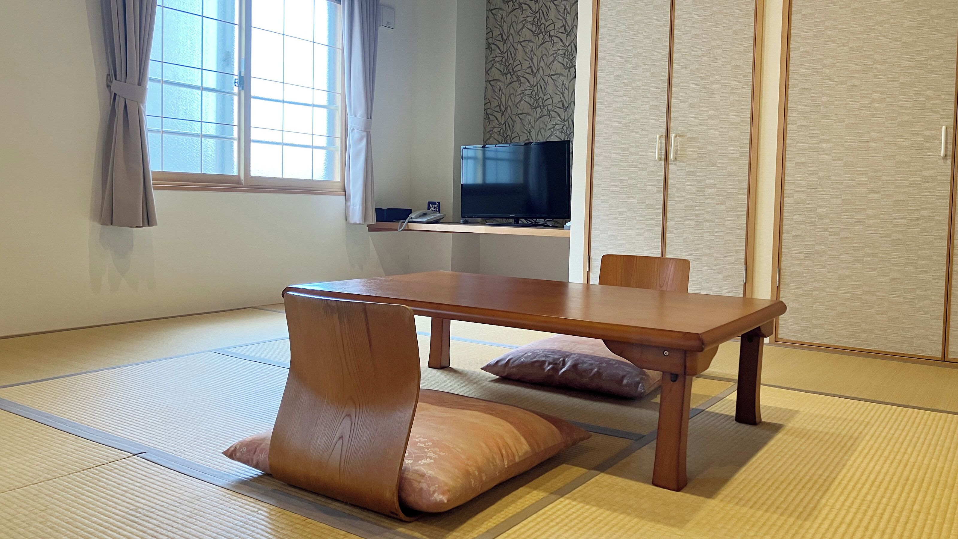 Ett traditionellt japanskt rum med tatamimattor på golvet, ett lågt bord, kuddar, en tv och skjutdörrar.