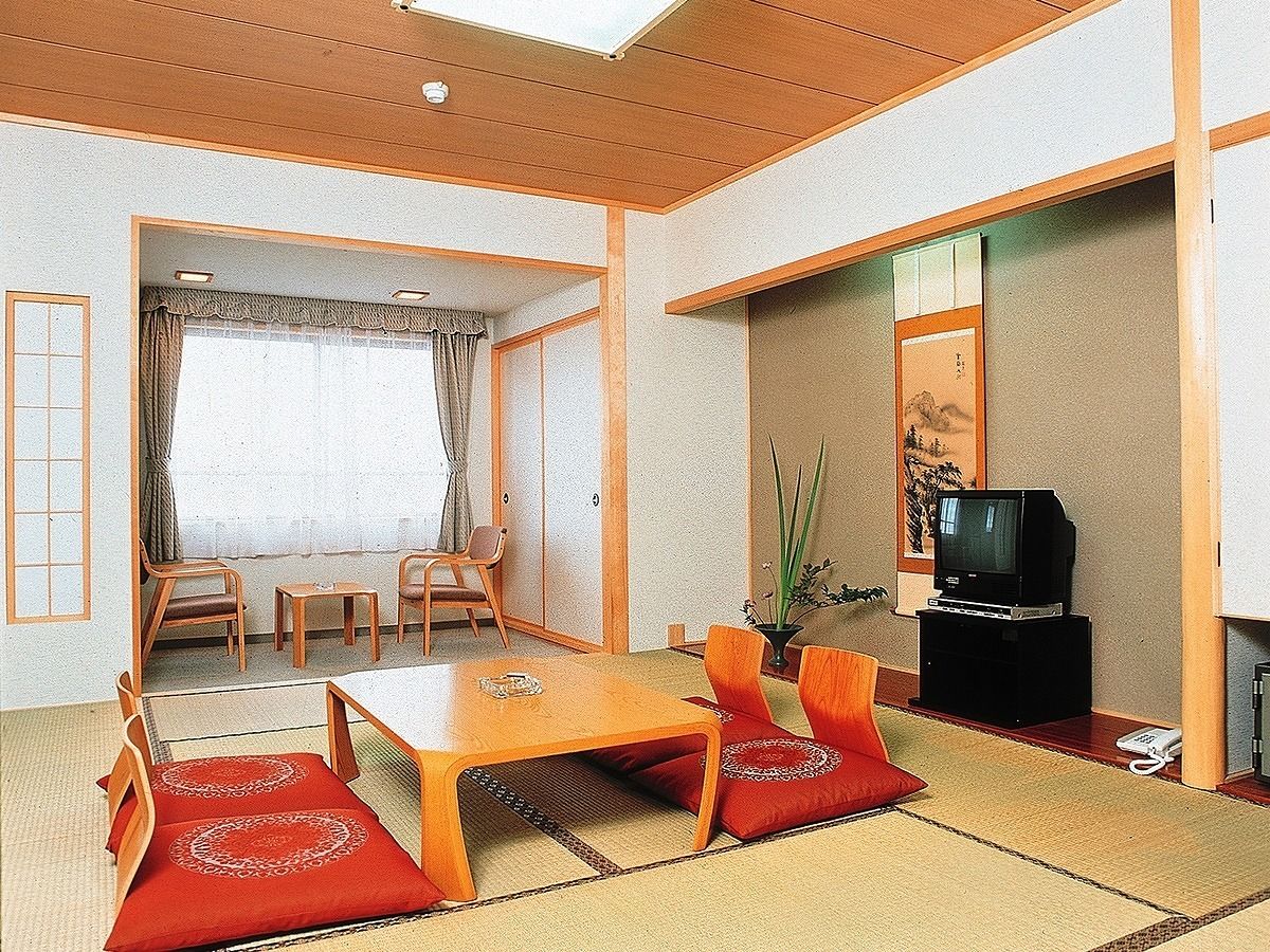 Un salon de style japonais traditionnel, avec un sol recouvert de tatamis, une basse table en bois et des coussins rouges.