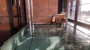 Zwembad met glazen bodem, met een houten bankje en een kleine tafel, omgeven door houten wanden en grote ramen.