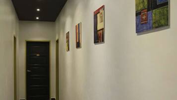 A hallway with a black door at the end, recessed lighting, and framed artwork on the walls.