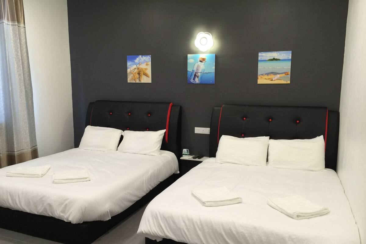 Dos camas individuales con sábanas blancas, cabeceros negros con detalles rojos y una lámpara fijada a la pared.