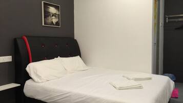 A neatly made bed with white linens and two folded towels, a black headboard with red accents, a wall-mounted light fixture, and a framed picture above the bed.