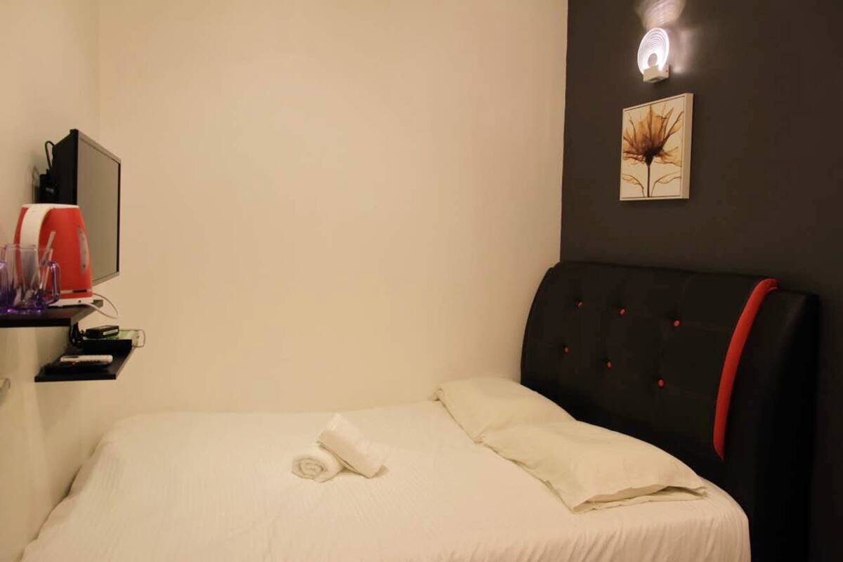 Una cama bien tendida con una toalla enrollada, una mesita de noche con una lámpara y un cuadro colgado en la pared.
