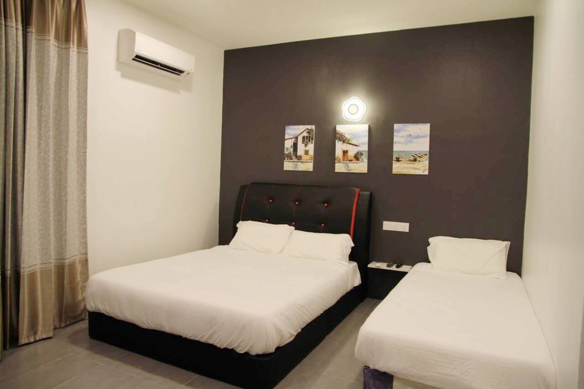Una habitación de hotel con dos camas individuales, un cabecero oscuro y tres cuadros colgados en la pared.