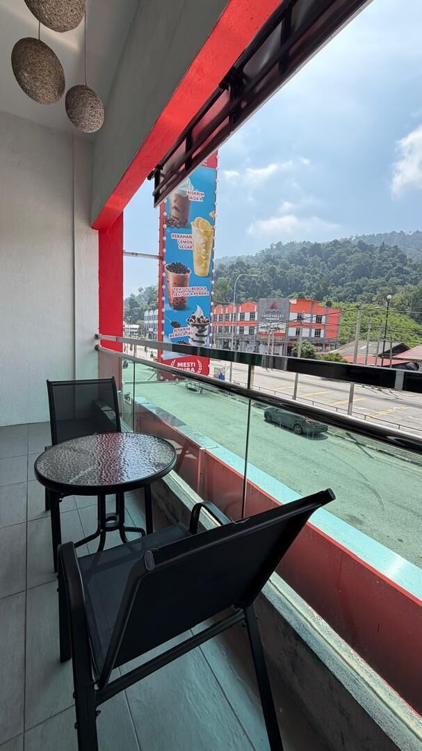 Un balcón con mesa y sillas, vista a una carretera y edificios, y un anuncio grande.