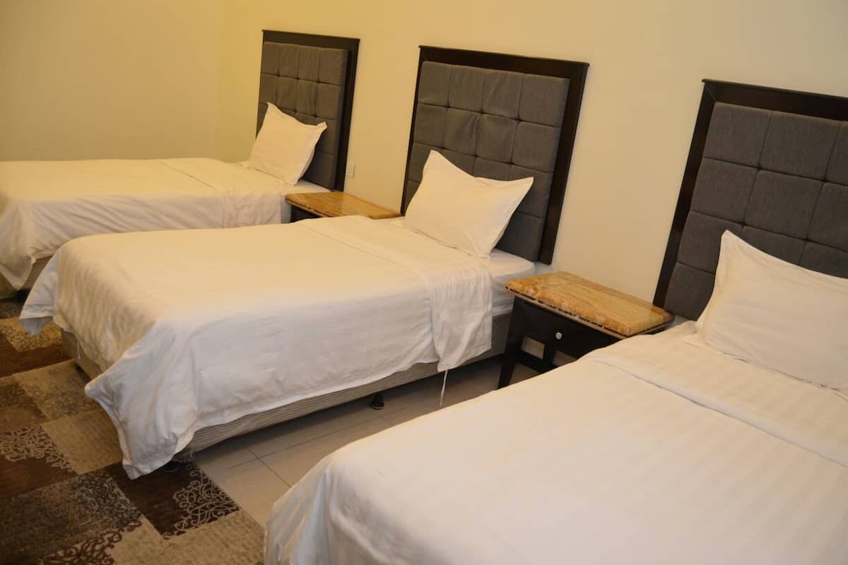 Une chambre d’hôtel avec trois lits simples, chacun doté d’une table de chevet en bois et d’une tête de lit.