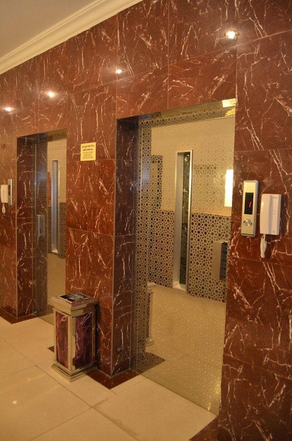 A marble-floored lobby with a reception desk, a trash bin, and a digital phone on the wall.