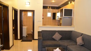 Una sala de estar con sofá y una mesita de centro, una cocina con microondas y refrigerador, y un baño con inodoro y lavamanos.