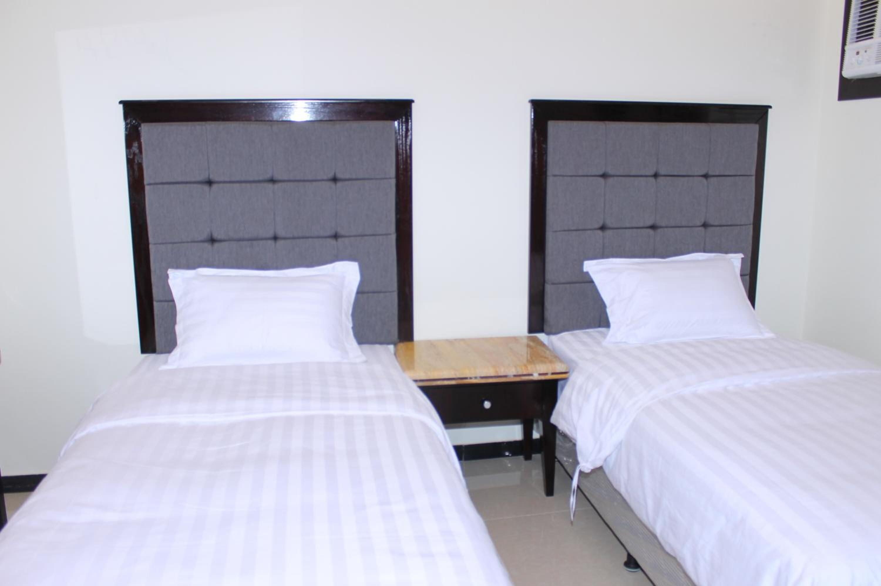 A hotel room with two single beds, a wooden nightstand, and a wall-mounted air conditioning unit.