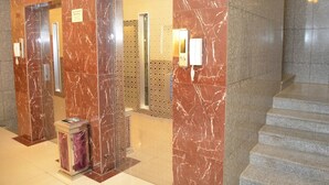 Un hall con suelo de mármol, un mostrador de recepción, un ascensor con paredes de vidrio y una escalera.