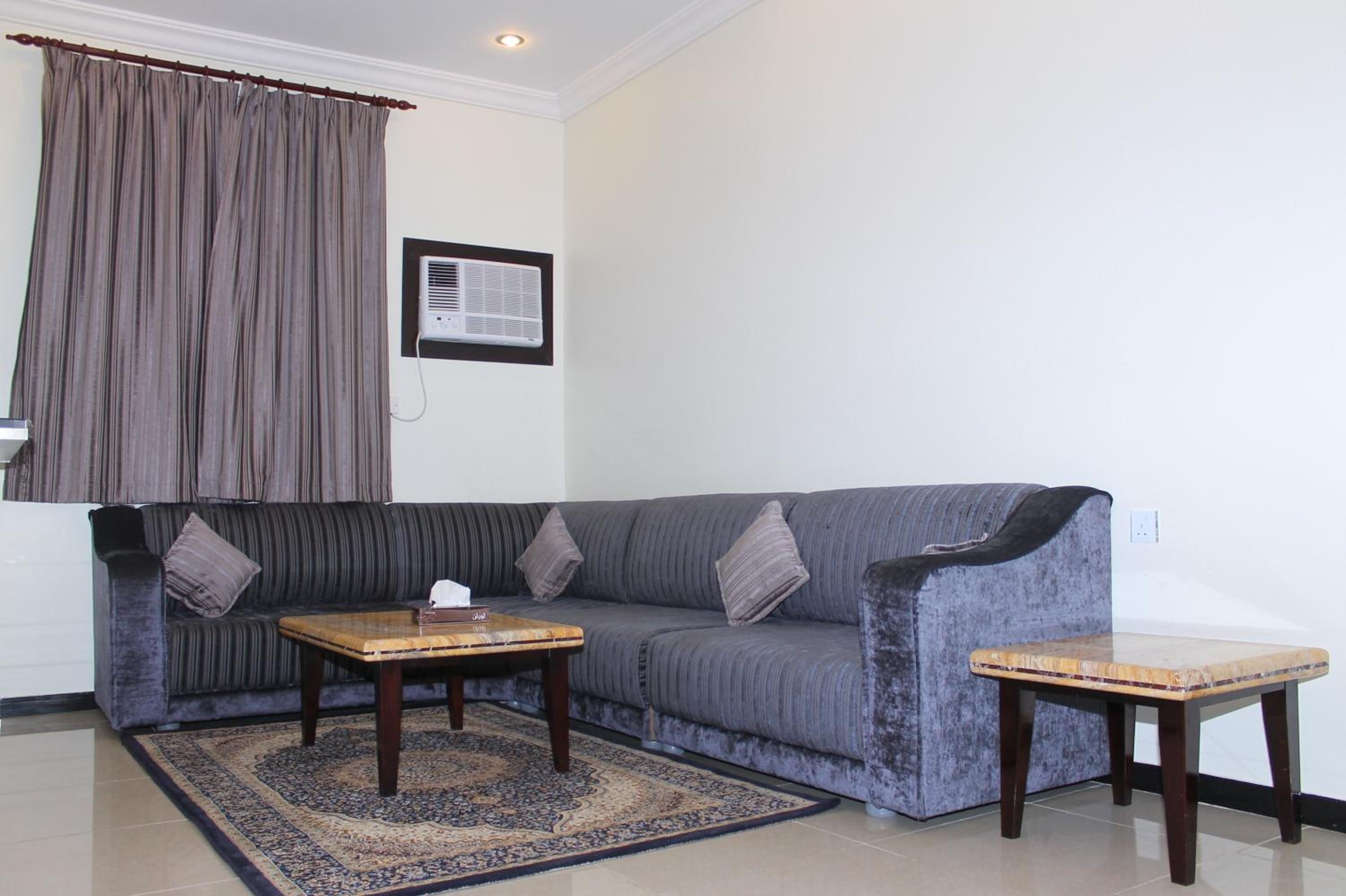 A living room with a grey sofa, two wooden side tables, a patterned rug, and a wall-mounted air conditioner.