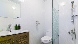 Une salle de bain avec des toilettes blanches, une cabine de douche en verre et un meuble-lavabo en bois doté d’un miroir.