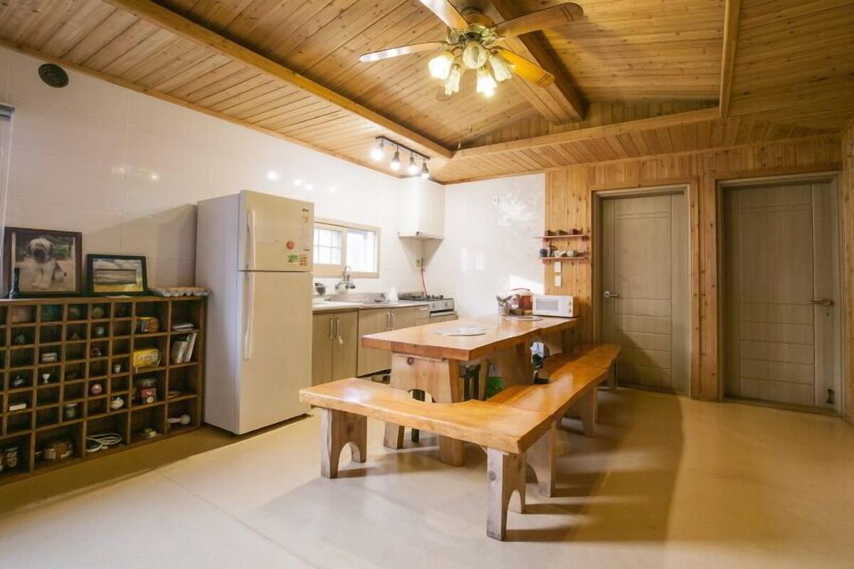 Una cocina con armarios de madera, un refrigerador, un banco de madera y un ventilador de techo.